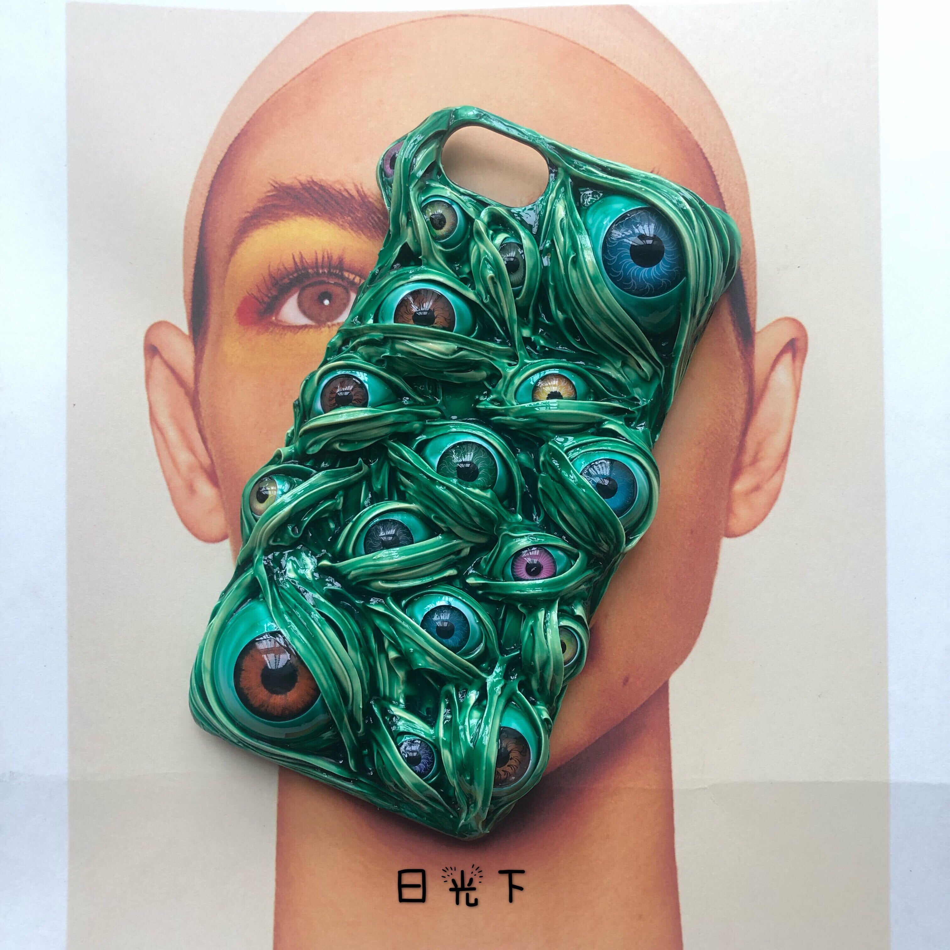 A 3D green phone case covered in realistic eyeballs, displayed against a portrait background.