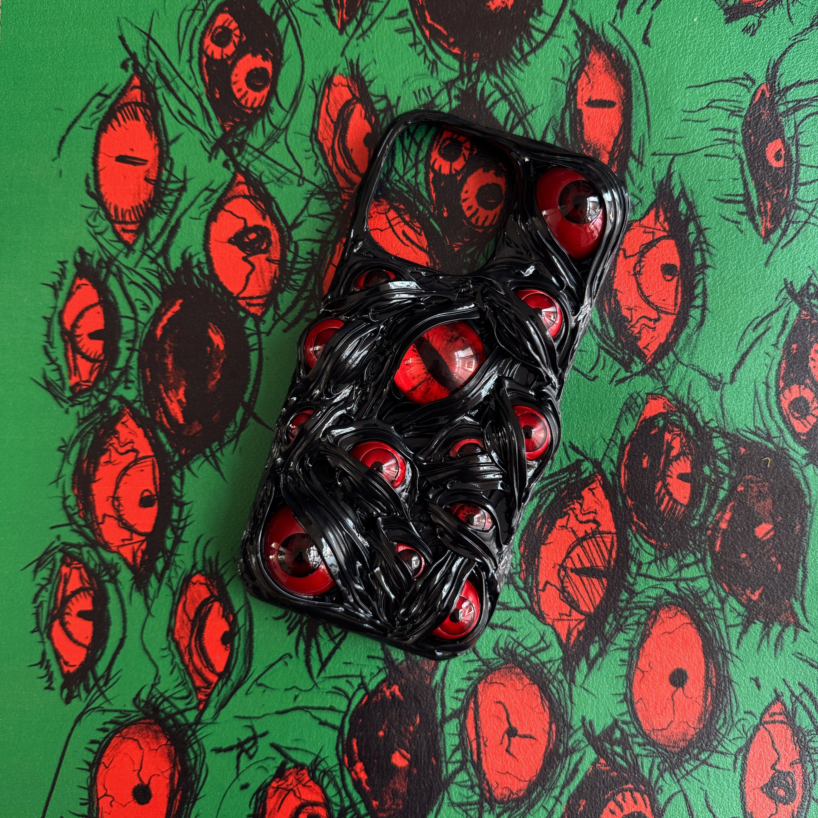 Handmade 3D black cream glue iPhone case featuring multiple realistic red eyes on a green eye-pattern background.