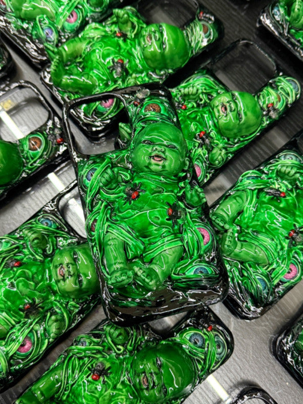 A surreal 3D green baby doll phone case with eyes and insects, resting on a pile of plastic baby doll parts.