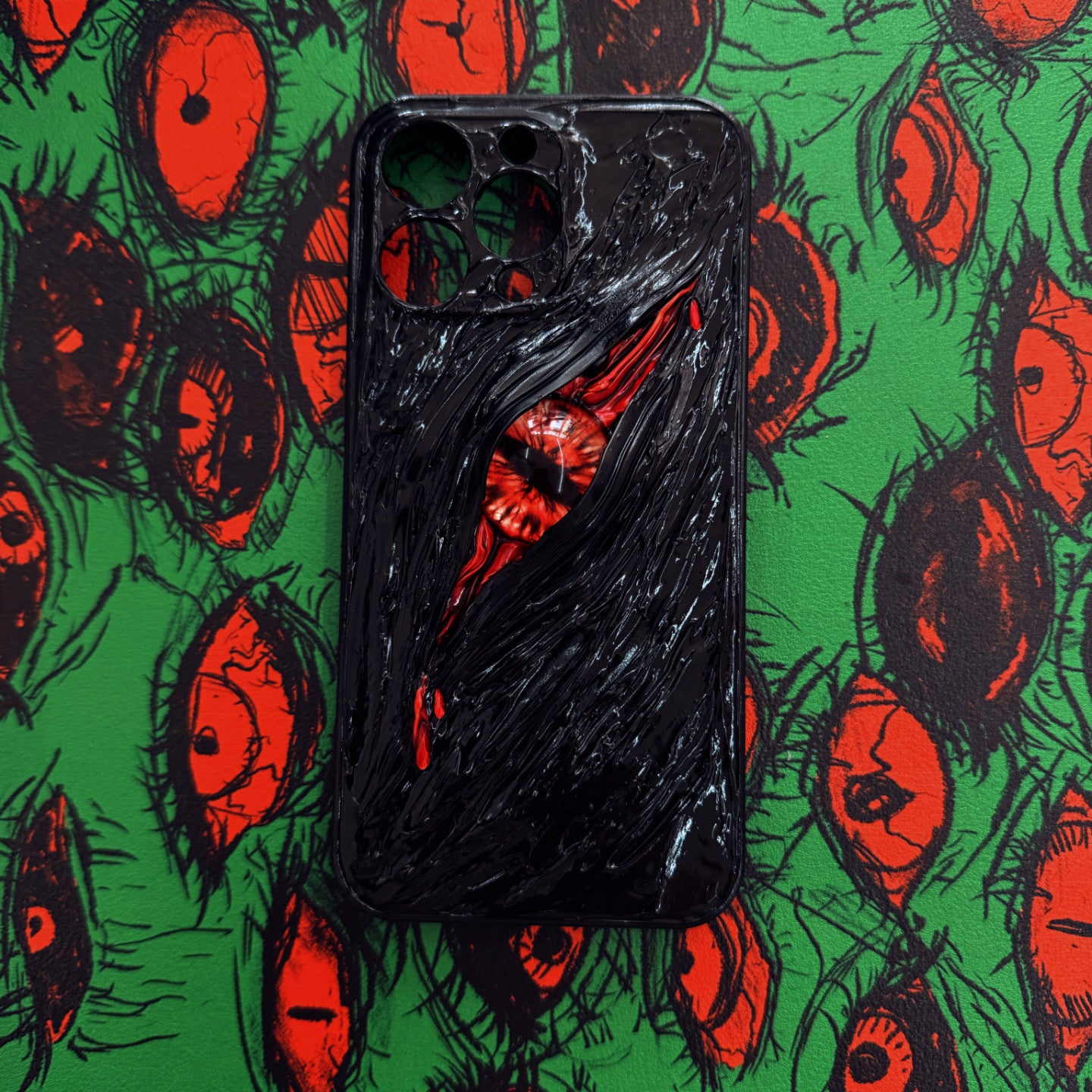 A gothic-style iPhone case featuring a realistic, textured eye design with black and red details, set against a green background with multiple eye illustrations.