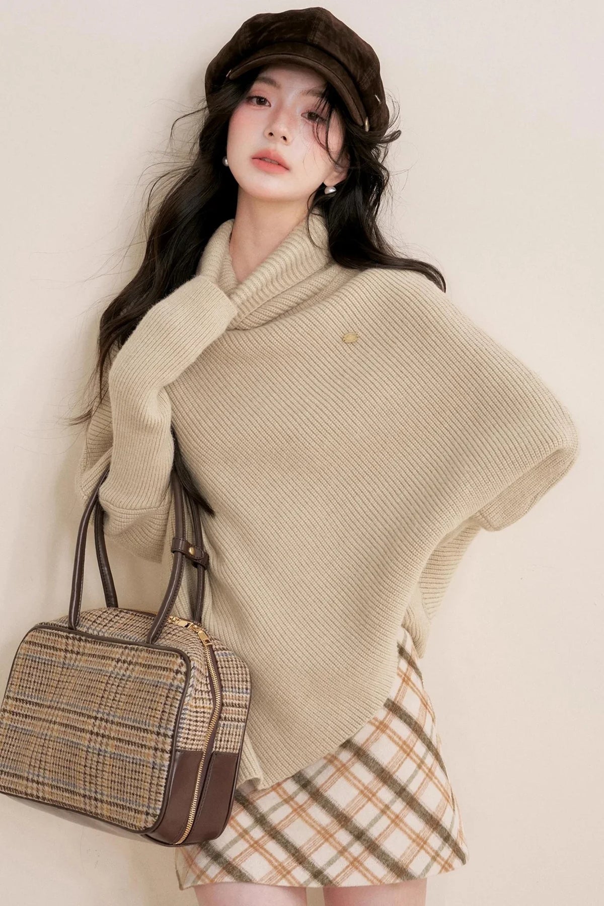 An oatmeal-colored asymmetrical cape sweater with a turtleneck.