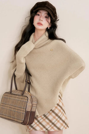 An oatmeal-colored asymmetrical cape sweater with a turtleneck.
