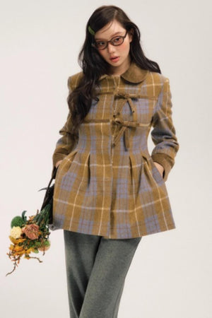 A woman wearing a turmeric plaid woolen coat with bow-tie closures.