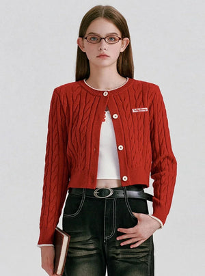 A woman wearing a red cable-knit cropped cardigan with white buttons.