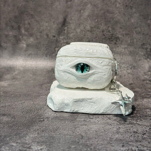 A white 3D textured AirPods case featuring a realistic glowing blue eye design with a star charm.