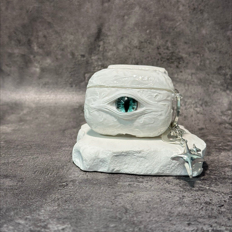A white 3D textured AirPods case featuring a realistic glowing blue eye design with a star charm.