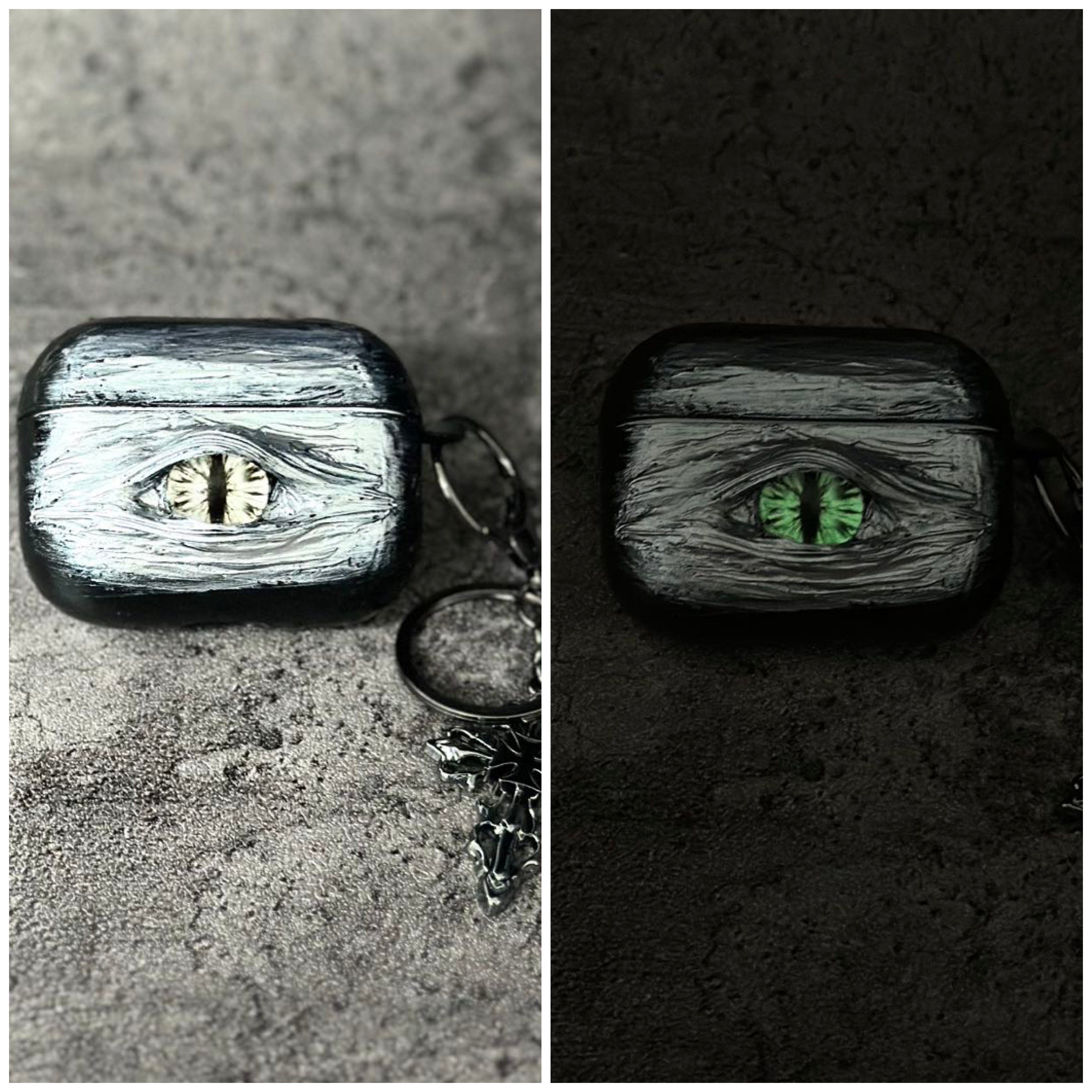 A white 3D textured AirPods case featuring a realistic glowing blue eye design with a star charm.