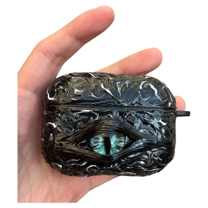 A white 3D textured AirPods case featuring a realistic glowing blue eye design with a star charm.