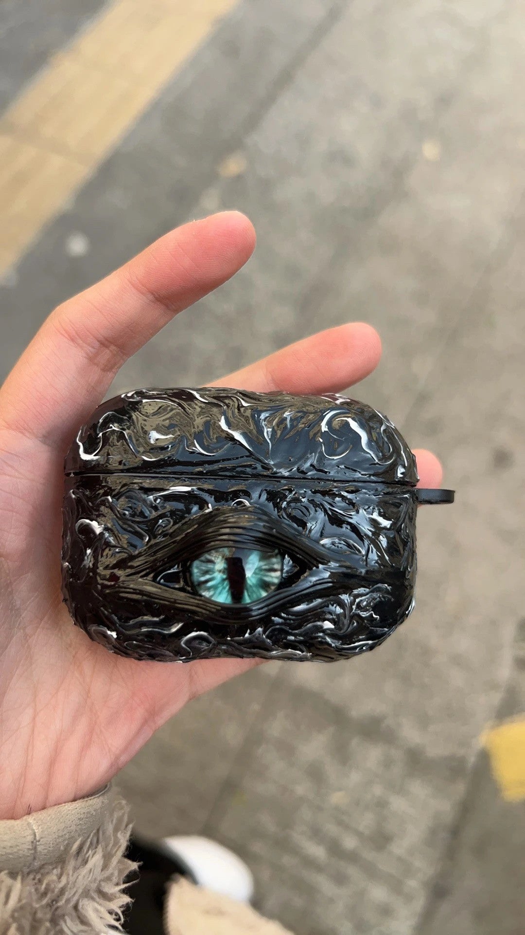 A white 3D textured AirPods case featuring a realistic glowing blue eye design with a star charm.