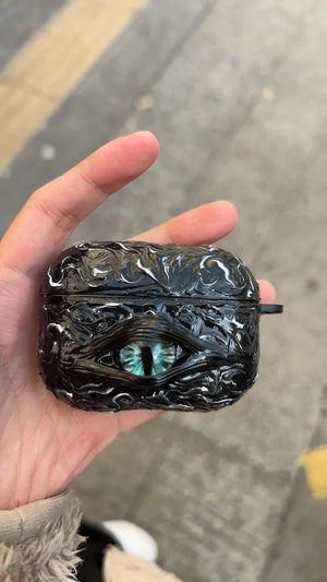 A white 3D textured AirPods case featuring a realistic glowing blue eye design with a star charm.