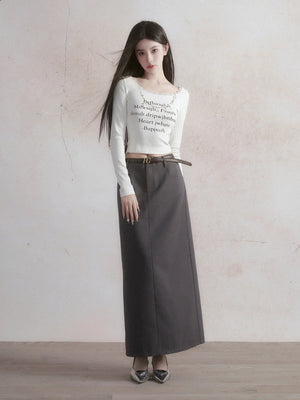 A woman wearing a long gray straight skirt with a white long-sleeve top.