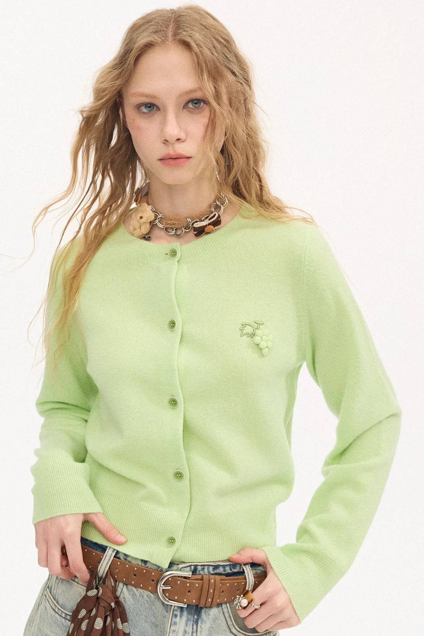 A woman wearing a light green wool sweater with grape embroidery.