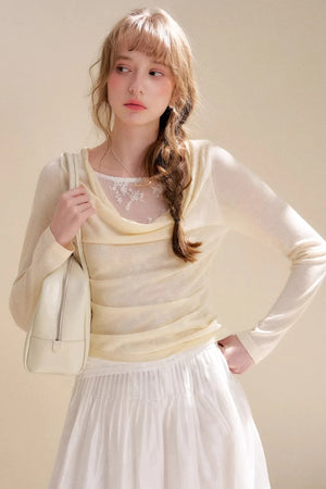 A woman wearing a vanilla-colored cowl neck sweater with lace detailing.
