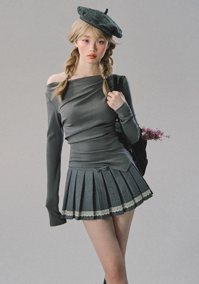A woman wearing a gray long-sleeve top and a pleated skirt.