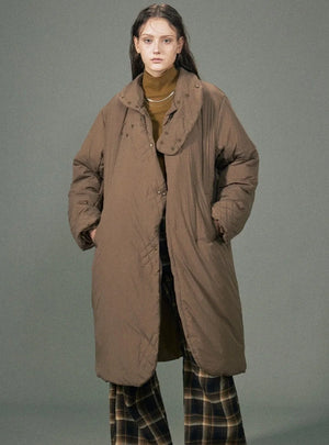 A woman wearing a long brown quilted puffer jacket with a stand-up collar.