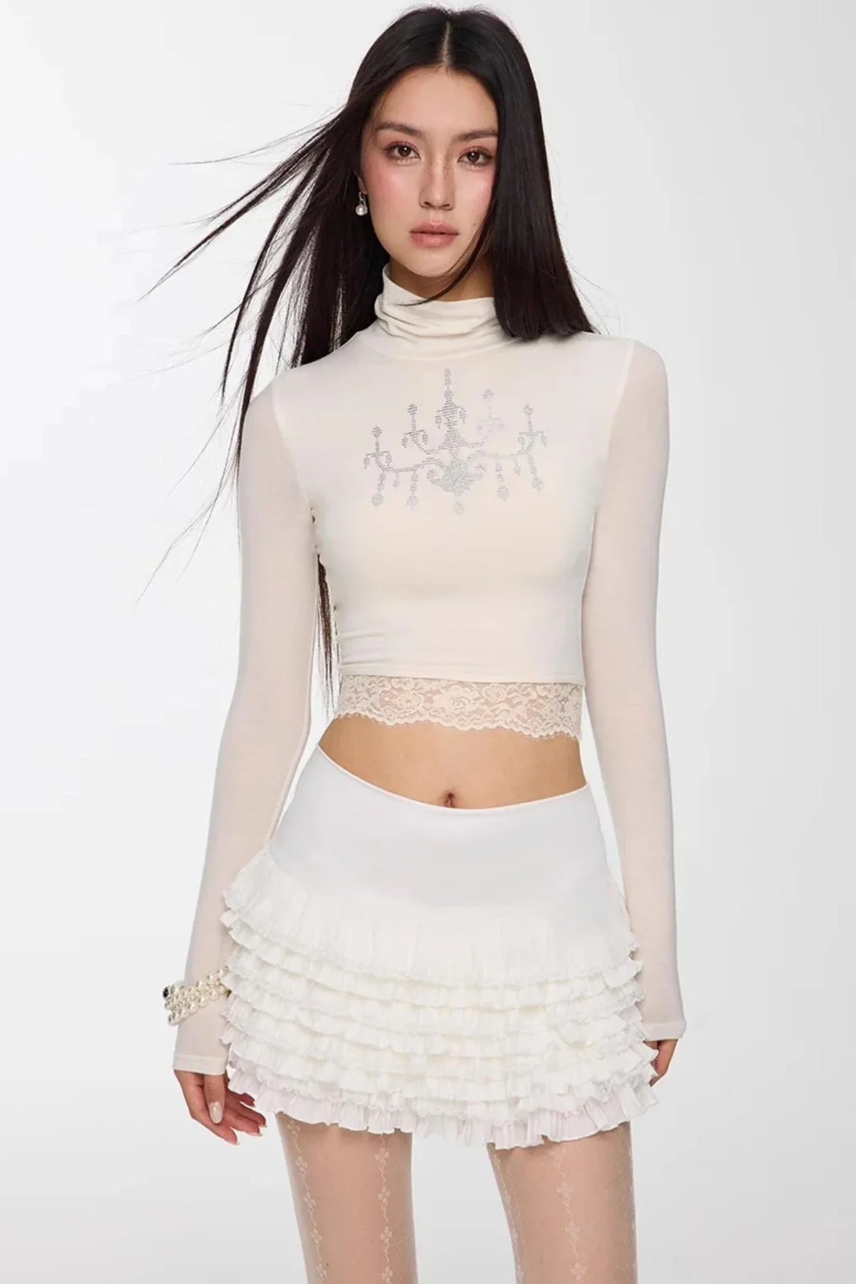 A woman wearing a white high-neck top with rhinestone detail.