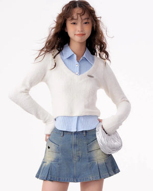 A woman wearing a white V-neck knit top layered over a blue shirt.