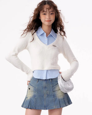 A woman wearing a white V-neck knit top layered over a blue shirt.