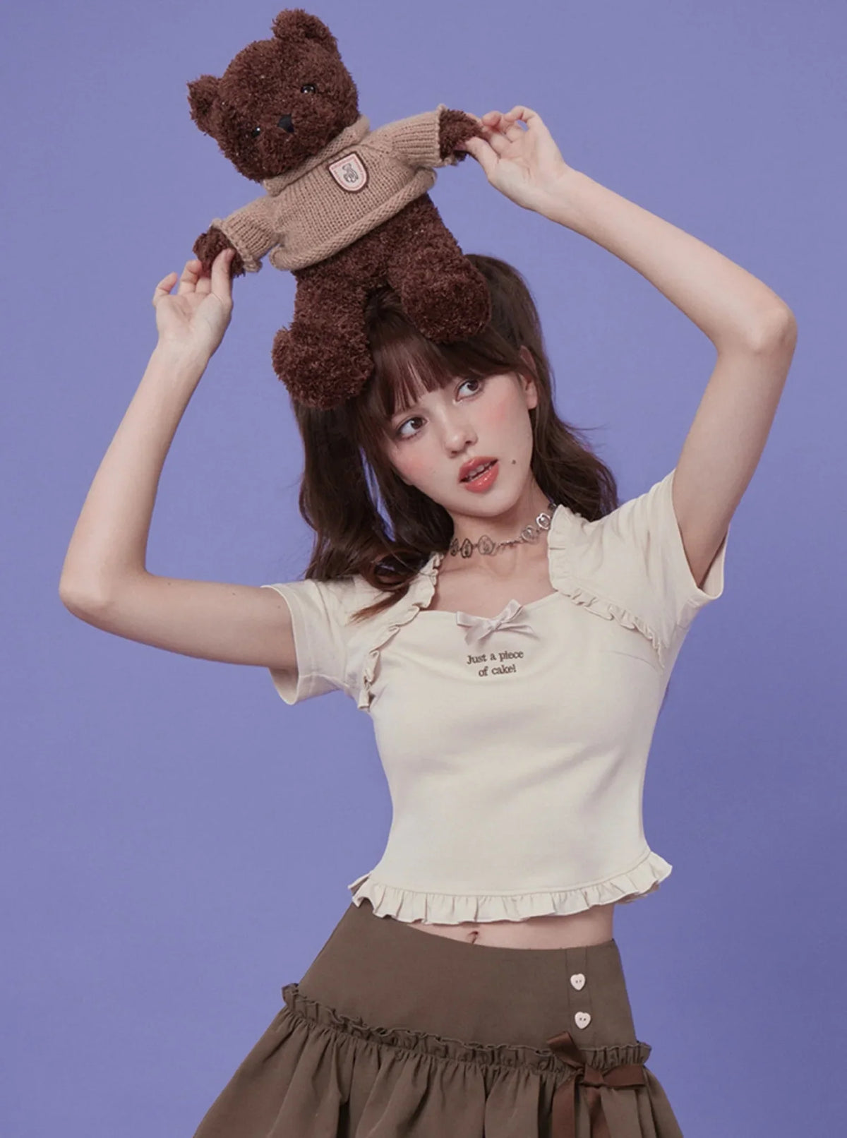 A light apricot square neck top with a bow detail and graphic text, styled with a brown skirt.