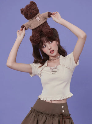 A light apricot square neck top with a bow detail and graphic text, styled with a brown skirt.