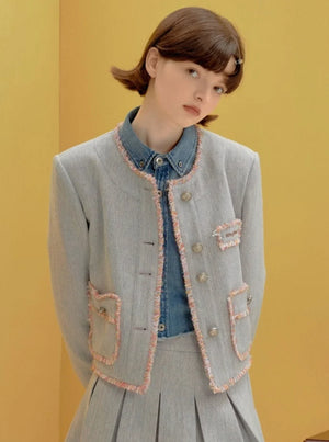 A woman wearing a light blue cropped jacket with fringe trim and matching skirt.