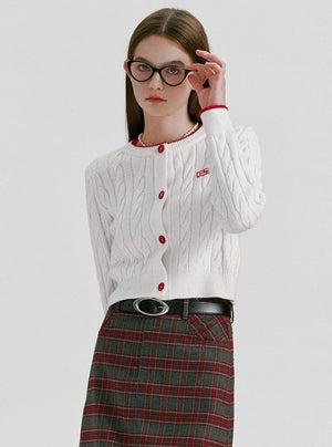 A woman wearing a red cable-knit cropped cardigan with white buttons.