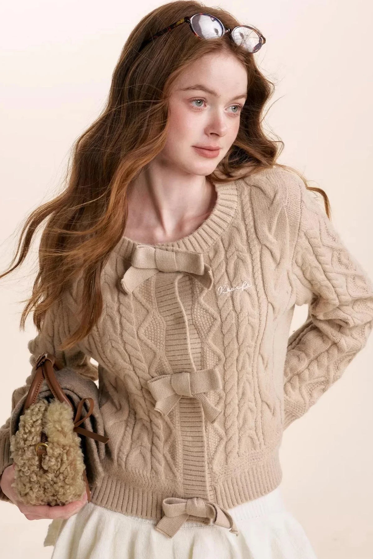 An oatmeal-colored cable-knit cardigan with bow accents.