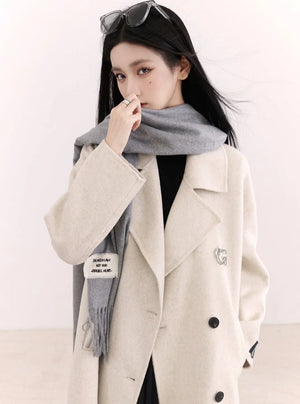 A woman wearing a beige double-breasted wool coat with a gray scarf.