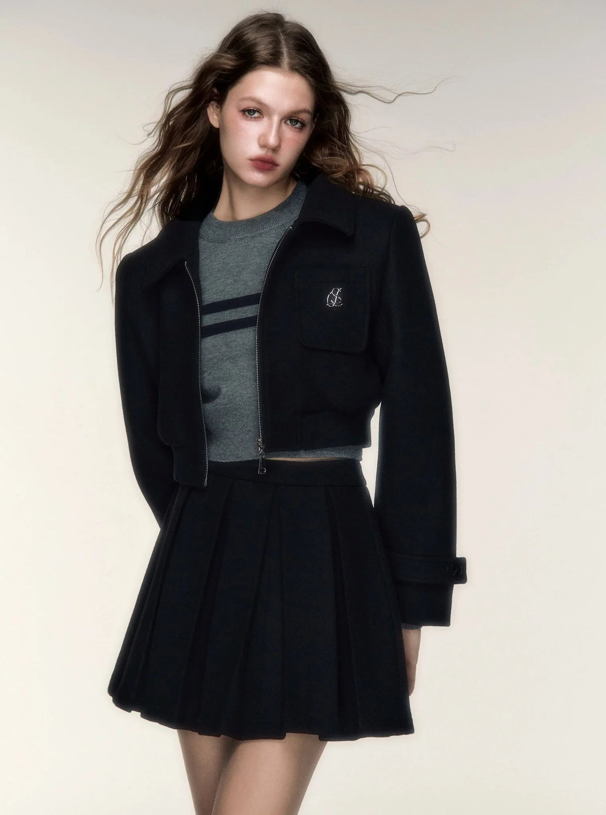A woman wearing a black woolen short jacket and matching pleated skirt set.