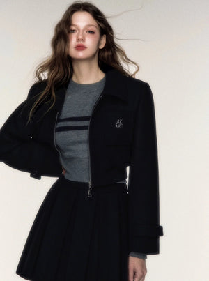 A woman wearing a black woolen short jacket and matching pleated skirt set.