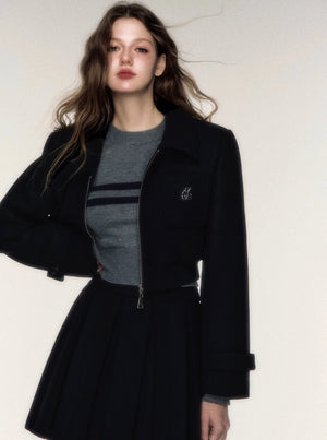 A woman wearing a black woolen short jacket and matching pleated skirt set.